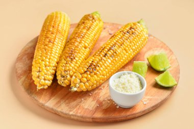 Lezzetli ızgara mısır koçanları ve turuncu arka planda bir kase peynirli ahşap tahta.