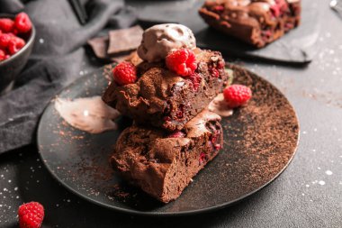 Üzerinde ahududulu çikolatalı kek ve siyah arka planda dondurma olan bir tabak.