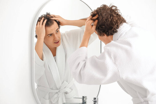 Молодой человек с потерей волос возле зеркала в ванной комнате