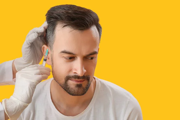 Handsome man receiving injection for hair growth on yellow background, closeup