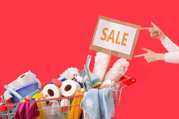 掃除用品や単語でいっぱいのショッピングカートを持つ女性赤い背景で販売 — ストック写真