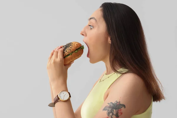 Νεαρή Γυναίκα Τρώει Νόστιμο Burger Στο Φως Φόντο Closeup — Φωτογραφία Αρχείου