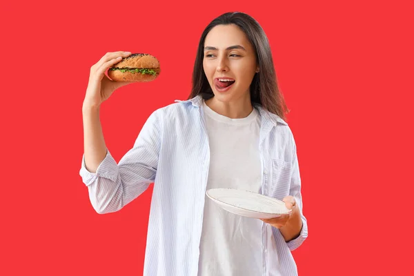 Młoda Kobieta Smacznym Burgerem Czerwonym Tle — Zdjęcie stockowe