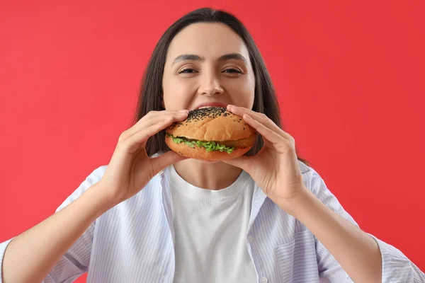 Mujer Joven Comiendo Sabrosa Hamburguesa Sobre Fondo Rojo Primer Plano —  Fotos de Stock