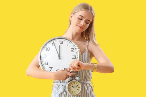 黄色の背景に腕時計を見て時計を持つ若い女性 締め切りの概念 — ストック写真