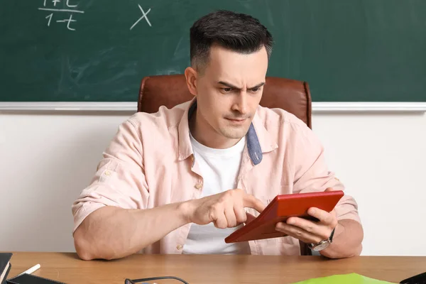 stock image Male Math teacher with calculator sitting at table in classroom