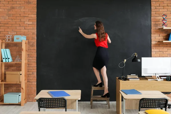 Female teacher writing on blackboard in classroom