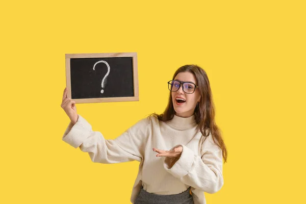 黄色の背景に疑問符で黒板を保持している女性教師 — ストック写真