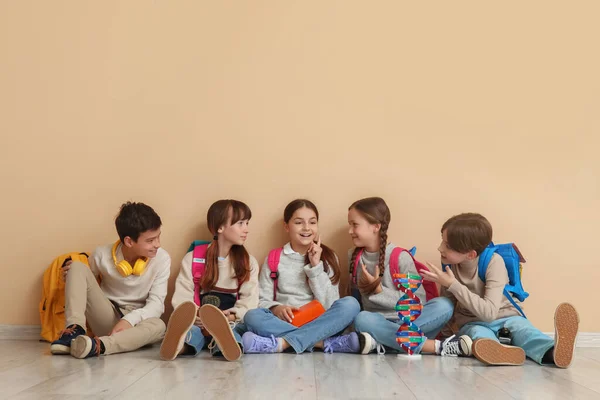Little pupils with backpacks sitting near beige wall