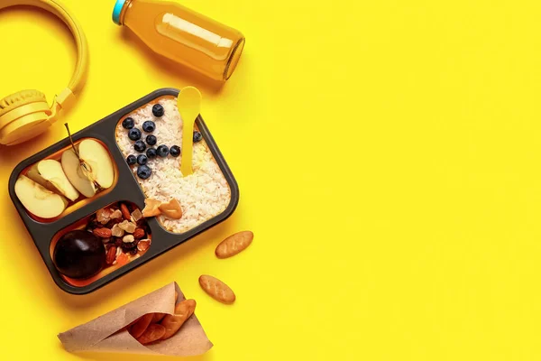 stock image Bottle of juice, headphones, crackers and lunchbox with tasty food on yellow background