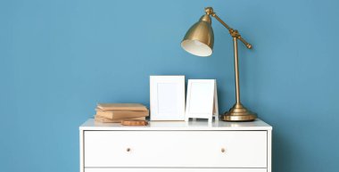 Boş çerçeveler, lamba ve mavi duvarın yanındaki çekmecelerin üstündeki kitaplar. Tasarım için pankart