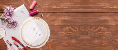 Tablolar, iplikler, leylak çiçekleri ve ahşap zemin üzerinde metin için yeri olan çember nakışlar.