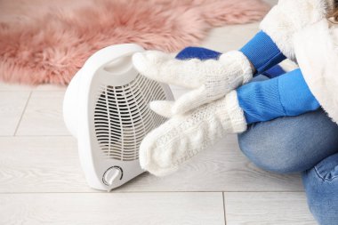 Evdeki elektrikli vantilatör ısıtıcısının yanında elleri ısıtan kadın, yakın çekim.