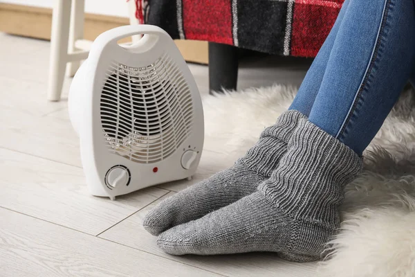 stock image Woman warming legs in socks near electric fan heater at home, closeup
