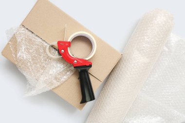 Gri arkaplanda bant, karton kutu ve baloncuk ambalajı paketleniyor