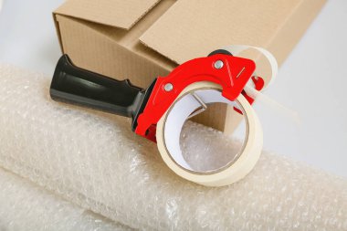 Gri arkaplanda bant, karton kutu ve baloncuk ambalajı paketleniyor