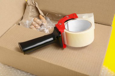 Sarı arkaplanda bant ve karton kutu paketleniyor