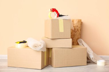 Paketleme bant dağıtıcısı, karton kutular ve baloncuk ambalajları bej duvarın yanında.