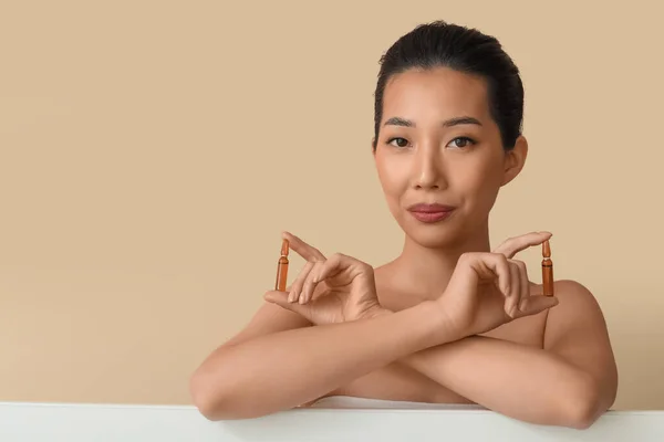 ベージュの背景にアンプルを持つ美しいアジアの女性 スキンケアコンセプト — ストック写真
