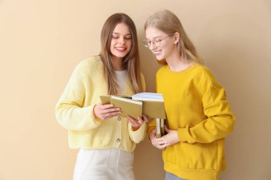 Mutlu bayan öğrenciler soluk sarı arka plan üzerine kitap okuyor.