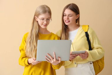 Soluk sarı arka planda dizüstü bilgisayarı ve tableti olan mutlu kız öğrenciler.