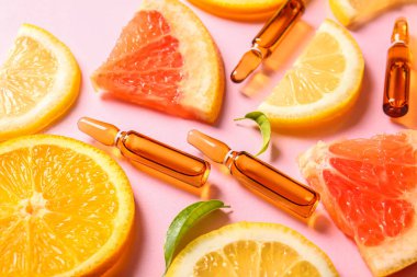 C vitamini ve pembe arka planda farklı narenciye dilimleri olan ampuller.