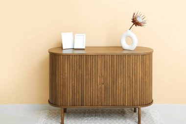 Protea çiçekli ahşap çekmeceler ve odada bej duvarın yanında boş resimler.