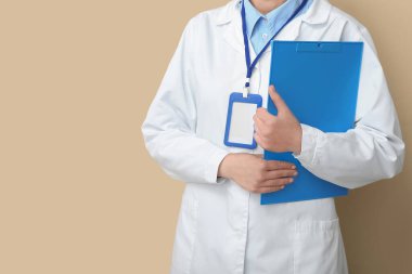 Bej arka planda rozeti ve panosu olan kadın doktor.