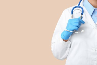 Steteskop ve bej arka planda tıbbi eldivenleri olan kadın doktor.