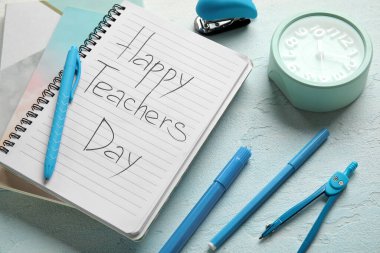 Yazılı defterler Mutlu Öğretmenler Günü, alarmlı saat ve grunge mavi gradyan arkaplan üzerindeki farklı kırtasiye