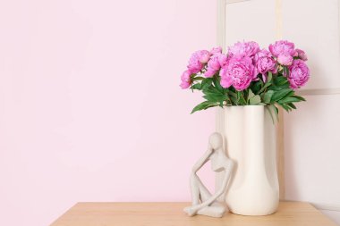 Rafların üzerinde pembe şakayık ve biblo vazosu ve renk duvarına yakın giyinme ekranı var.