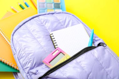 Sırt çantası boş defter ve sarı zemin üzerinde farklı kırtasiye malzemesi.