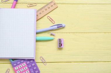 Sarı tahta zemin üzerinde farklı kırtasiye malzemesi ve hesap makinesi olan boş bir defter