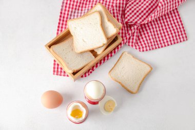 Haşlanmış tavuk yumurtası ve beyaz arka planda ahşap ekmek kutusu olan tutucular.