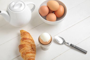 Haşlanmış tavuk yumurtası, çaydanlık ve ahşap kaplama kruvasan.