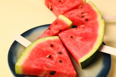 Sarı zemin üzerinde tatlı karpuz çubukları olan bir tabak.