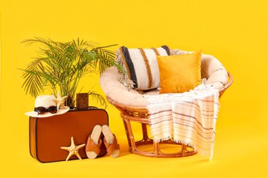 Sarı arka planda bavulu ve plaj aksesuarları olan rahat bir koltuk. Seyahat kavramı