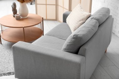 Beyaz tuğla duvarın yanında yastıklı ve sehpalı rahat gri kanepe.