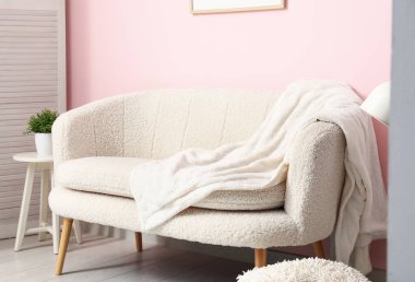 Pembe duvarın yanındaki rahat beyaz kanepe ve battaniye