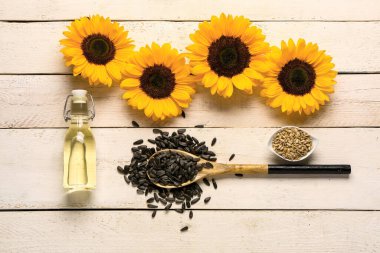 Ayçiçekleri, tohumlu kaşık ve hafif ahşap arka planda bir şişe yağ.