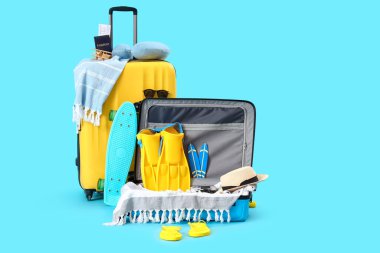 Kaykaylı bavullar ve mavi arka planda farklı plaj aksesuarları. Seyahat kavramı
