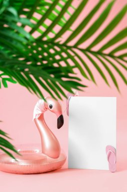 Flamingo şeklinde şişirilebilir yüzüklü boş poster ve pembe arka planda bitki yaprakları. Seyahat kavramı