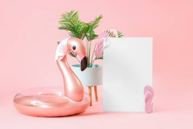 Flamingo şeklinde şişirilebilir yüzüklü boş poster ve pembe arka planda bitki yaprakları. Seyahat kavramı