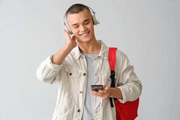 Mężczyzna Student Plecakiem Słuchawkach Pomocą Telefonu Komórkowego Szarym Tle — Zdjęcie stockowe