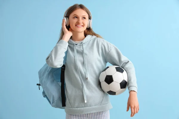 バックパックを持つ女性学生とサッカーボールリスニング音楽でヘッドフォンで青の背景 — ストック写真