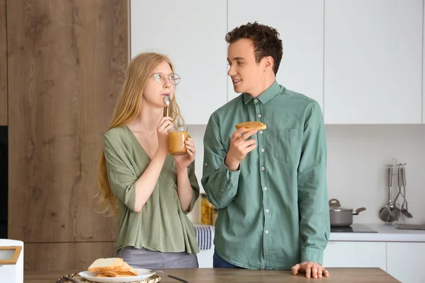 Young woman eating nut butter and handsome man with bread toast in kitchen