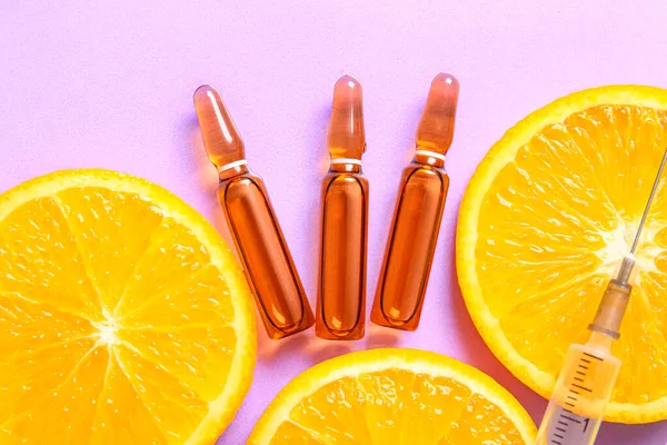 stock image Ampoules with vitamin C, syringe and orange slices on purple background, closeup