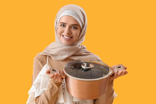 黄色の背景に鍋を調理するイスラム教徒の女性 — ストック写真