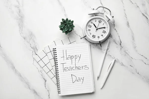 Notebook with text HAPPY TEACHERS DAY, alarm clock and pens on grunge white background
