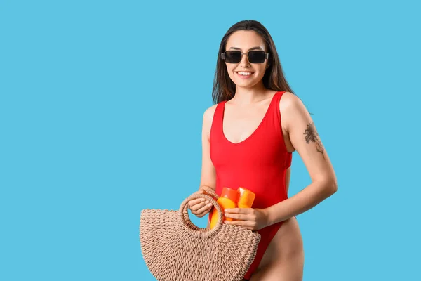 Junge Frau Mit Strandtasche Und Flaschen Sonnencreme Auf Blauem Hintergrund — Stockfoto